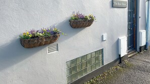 A building exterior with a sign reading 'The Boat House,' two flower planters, a door, and electrical boxes.