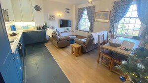 A modern living room with a sofa, a dining table, and a kitchen area with cabinets and a TV.