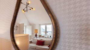Un espejo refleja una sala de estar con sofá, lámpara y candelabro.