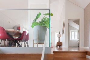 Un interior moderno con zona de comedor que incluye sillas rojas, una planta grande en maceta y una partición de vidrio.