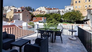 Una terraza con mobiliario exterior, una mesa y sillas, con vista a un paisaje urbano con edificios y árboles.