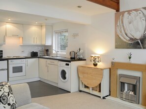 A modern kitchen with white cabinets, a washing machine, a coffee machine, and a fireplace. - Rosthwaite Annexe -UK32660 (Windmere)