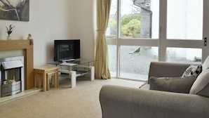 Una sala de estar con chimenea, televisor, sofá y ventanas grandes con cortinas.
