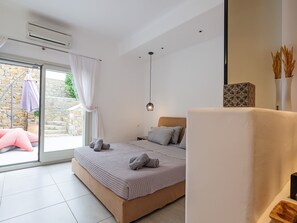 Un dormitorio moderno con una cama grande, una mesita de noche pequeña, una lámpara colgante y vistas a una pared de piedra y un espacio exterior.