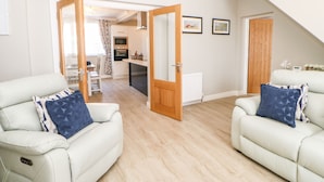 A modern living room with two white sofas, a wooden floor, and a kitchen in the background. - Lobster Pot Retreat (Newbiggin-by-the-Sea)