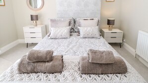 A neatly arranged bedroom with a large bed, two bedside tables, a round mirror, and two lamps. - Lobster Pot Retreat (Newbiggin-by-the-Sea)