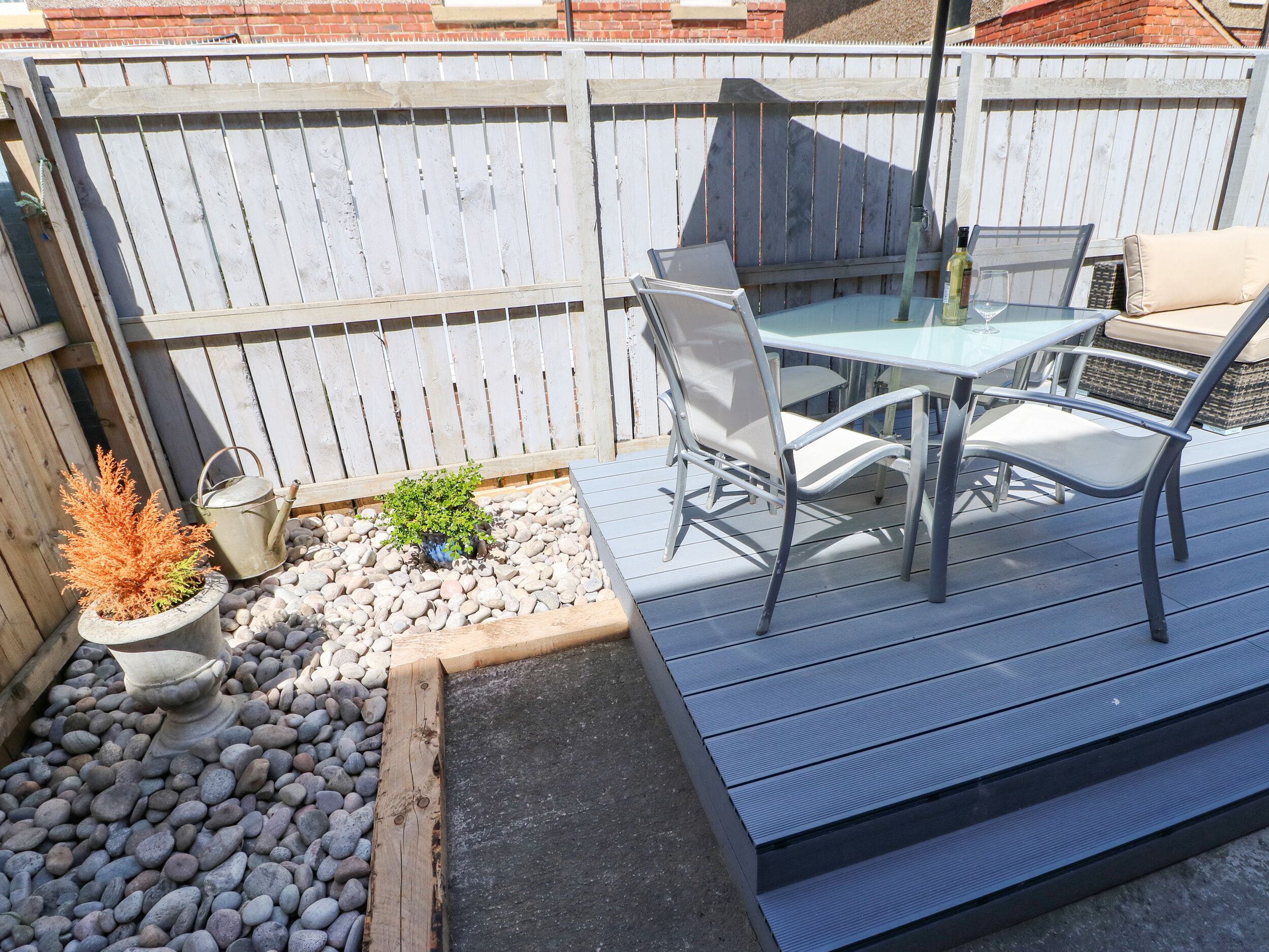A patio with a table and chairs, surrounded by a wooden deck and a brick wall.