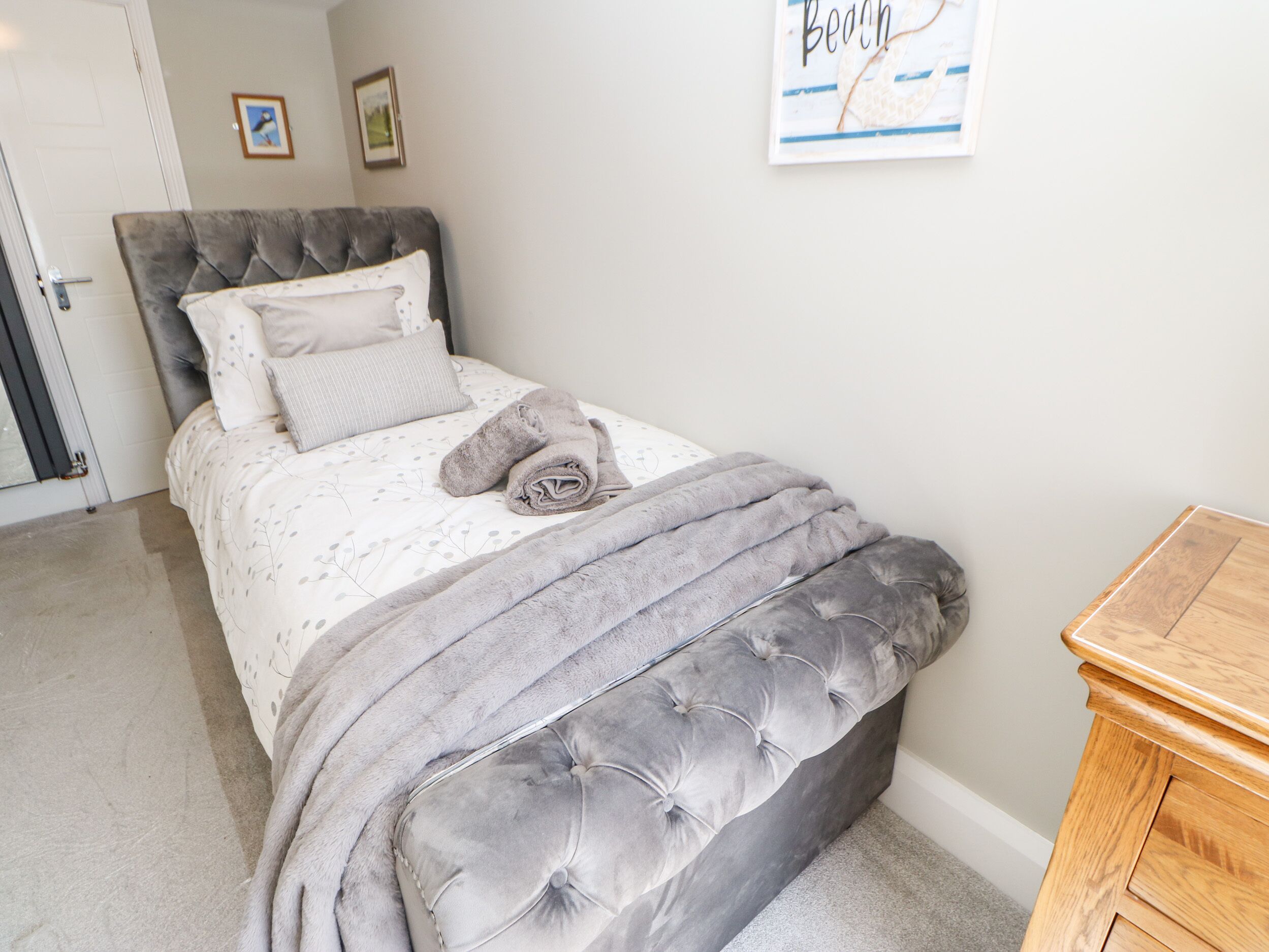 Ein Schlafzimmer mit einer gepolsterten Kopfstütze, einem Bett mit einem gemusterten Bettüberwurf, einem aufgerollten Handtuch und einem Holznachttisch.