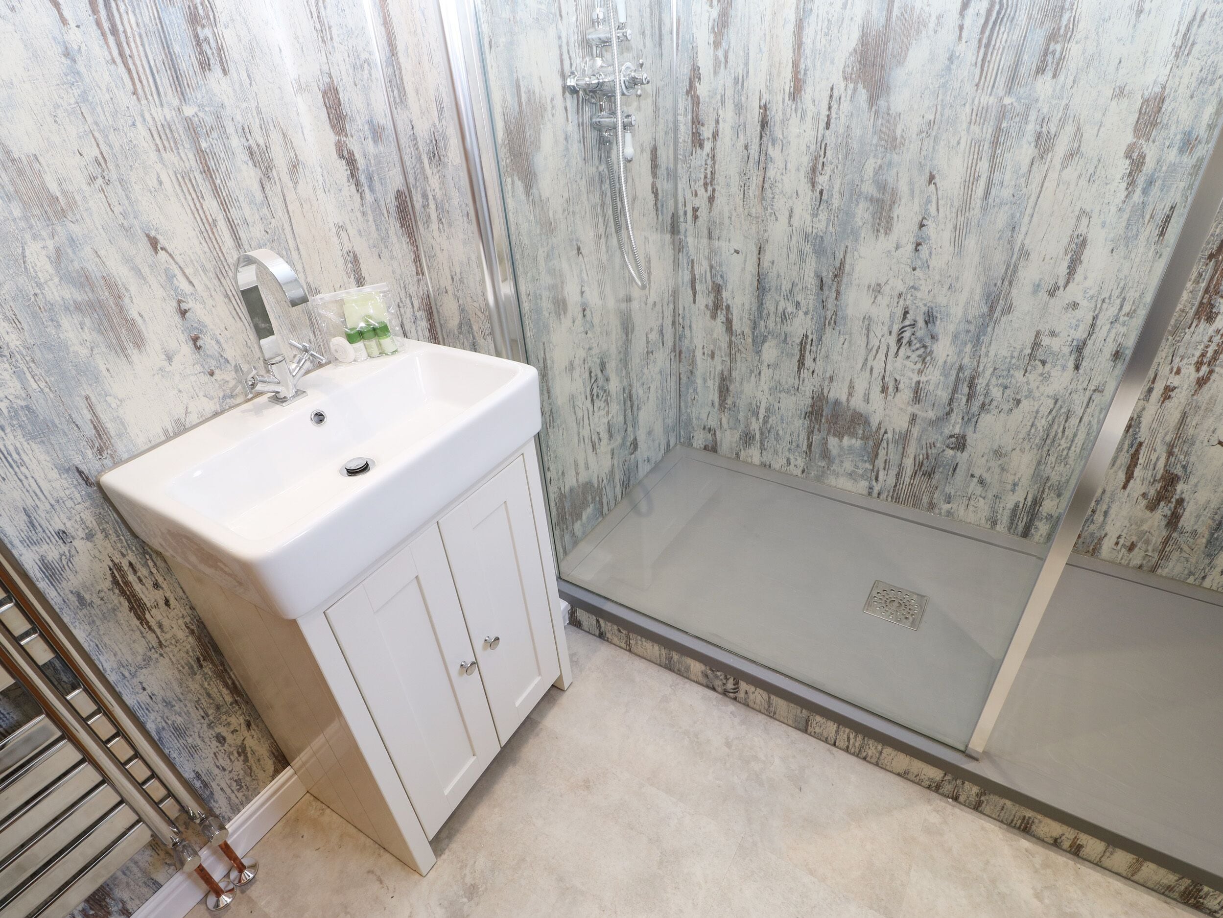 Een badkamer met een witte wastafel, een douche en een wand met een houtstructuur.