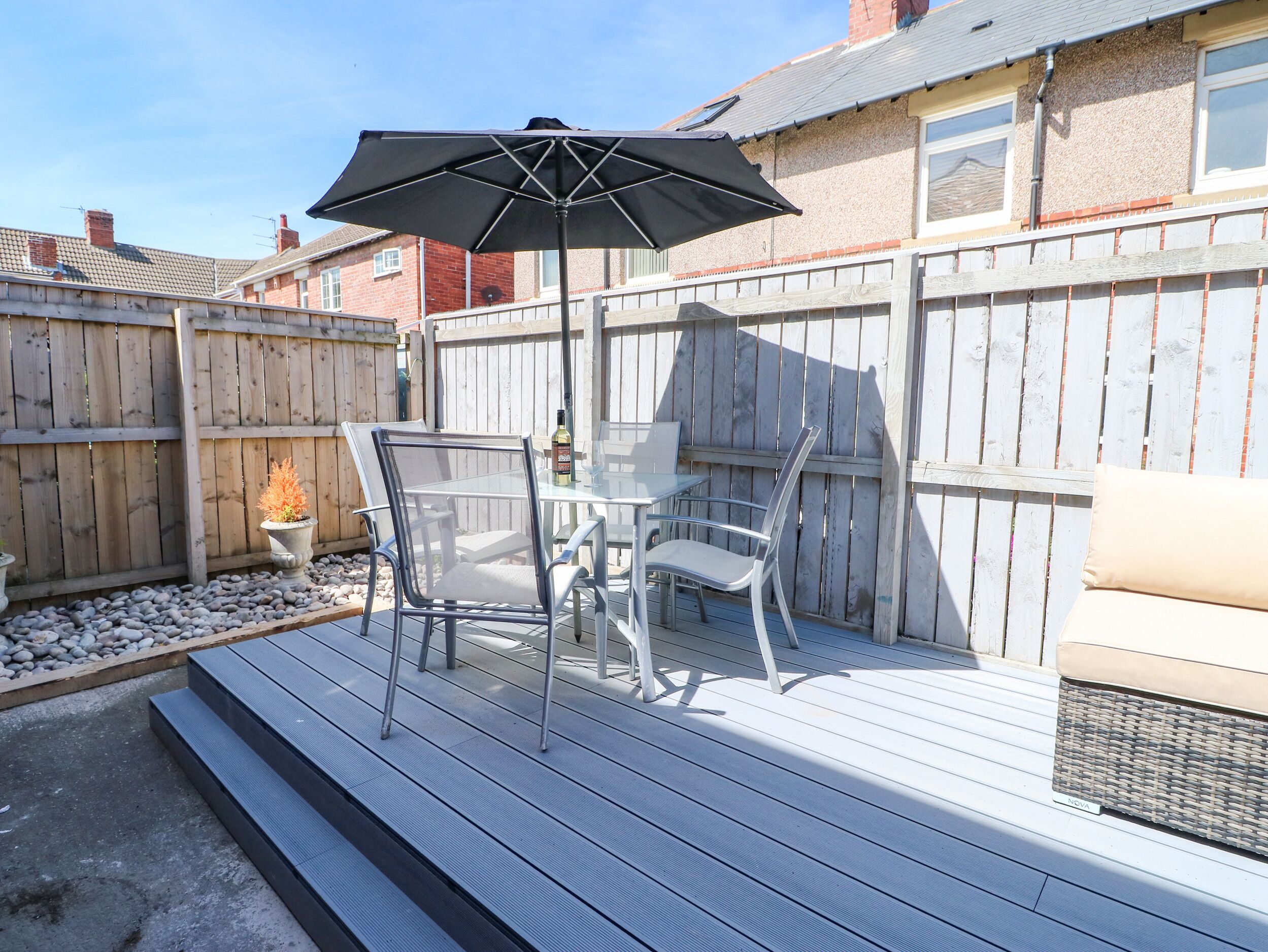 A patio with a table and chairs, a black umbrella, and a wooden deck.