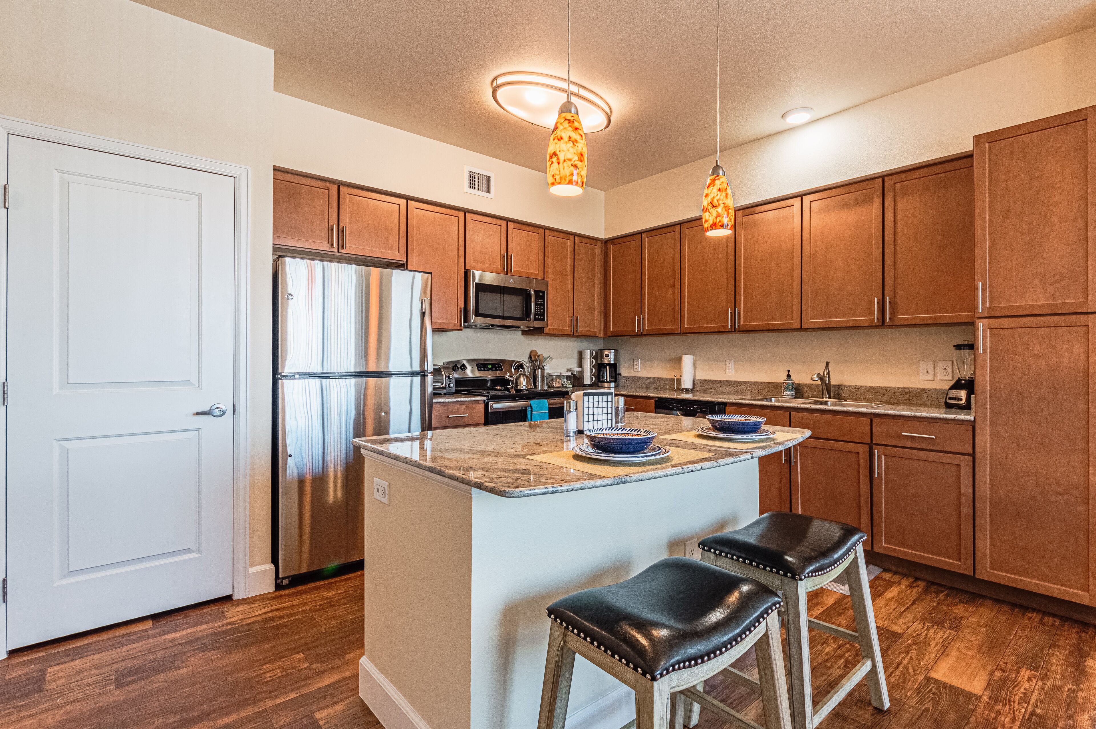 A modern kitchen with wooden cabinets, stainless steel appliances, and a central island with stools.