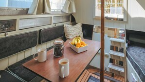 Een kleine keuken met een tafeltje, twee mokken, een koffiezetapparaat en een schaal met fruit.