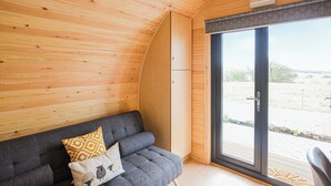 Una habitación acogedora con techo de madera, un sofá gris con cojines estampados y un amplio ventanal corredero que da a un espacio exterior.