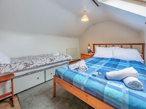 Un dormitorio con dos camas, una mesita de noche con lámpara y cabecera de madera.