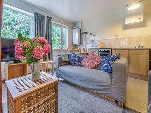 Un espacio habitable compacto con sofá, una mesita de madera, televisor, zona de cocina y ventana con cortinas.