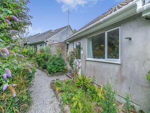 A residential property with a gravel driveway, a wooden fence, and a variety of plants and flowers.
