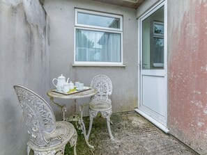 Un pequeño espacio al aire libre con una mesa y dos sillas, una ventana y una puerta.