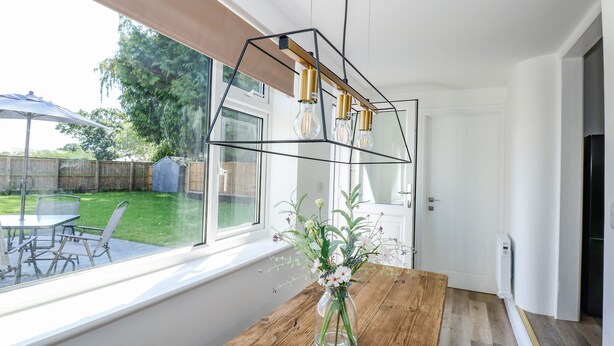 Une cuisine moderne avec une table en bois, un vase de fleurs et une grande fenêtre donnant sur un jardin.