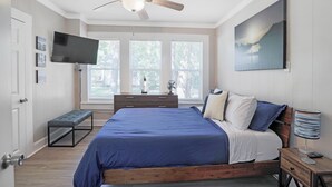 Una camera da letto con un letto, una ventola a soffitto, una TV e una finestra vista alberi.