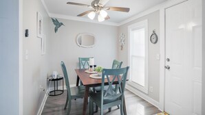 Zona pranzo con tavolo in legno, sedie color acquamarina, ventilatore a soffitto e una porta bianca.