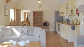 A cozy living room with a sofa, a wooden coffee table with tea set, and a kitchen with wooden cabinets and appliances. - Troed Y Rhiw Aberpoth (Aberporth)