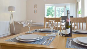 A dining area with a table set for four, a bottle of DINO Prosecco, and a view of a cozy living room with a sofa and a lamp. - Troed Y Rhiw Aberpoth (Aberporth)