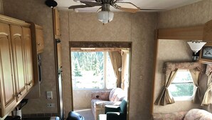 Een compact RV-interieur met een kitchenette, een plafondventilator, een raam met gordijnen en een bank.