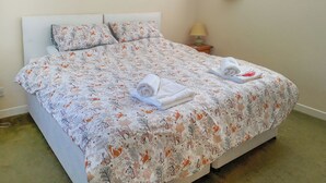 Een net opgemaakt bed met een bedspreider met dessin, een bedlampje en drie ingelijste foto's aan de muur.