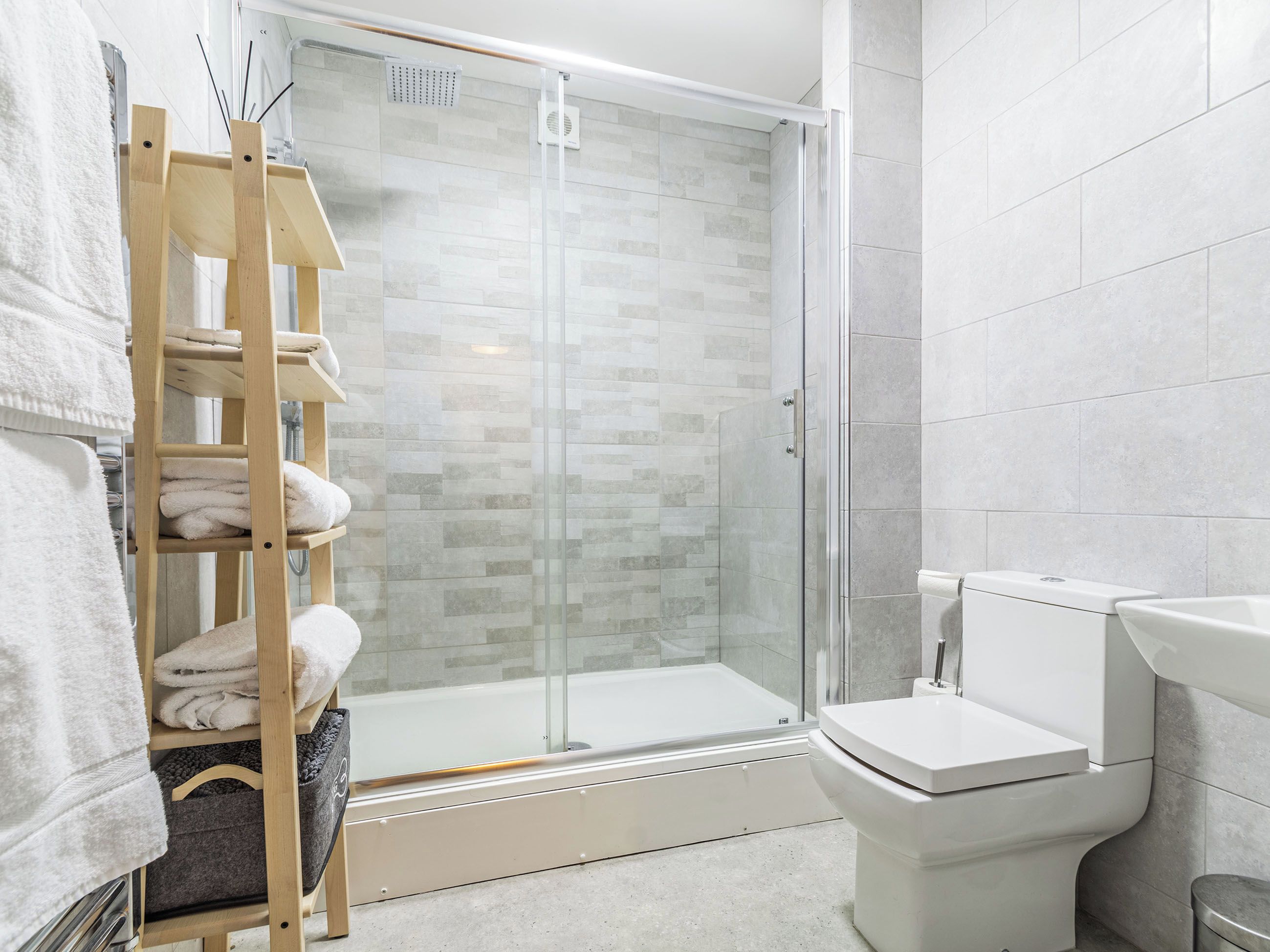 A modern bathroom with a glass-enclosed shower, a toilet, and a wooden towel rack with folded towels.