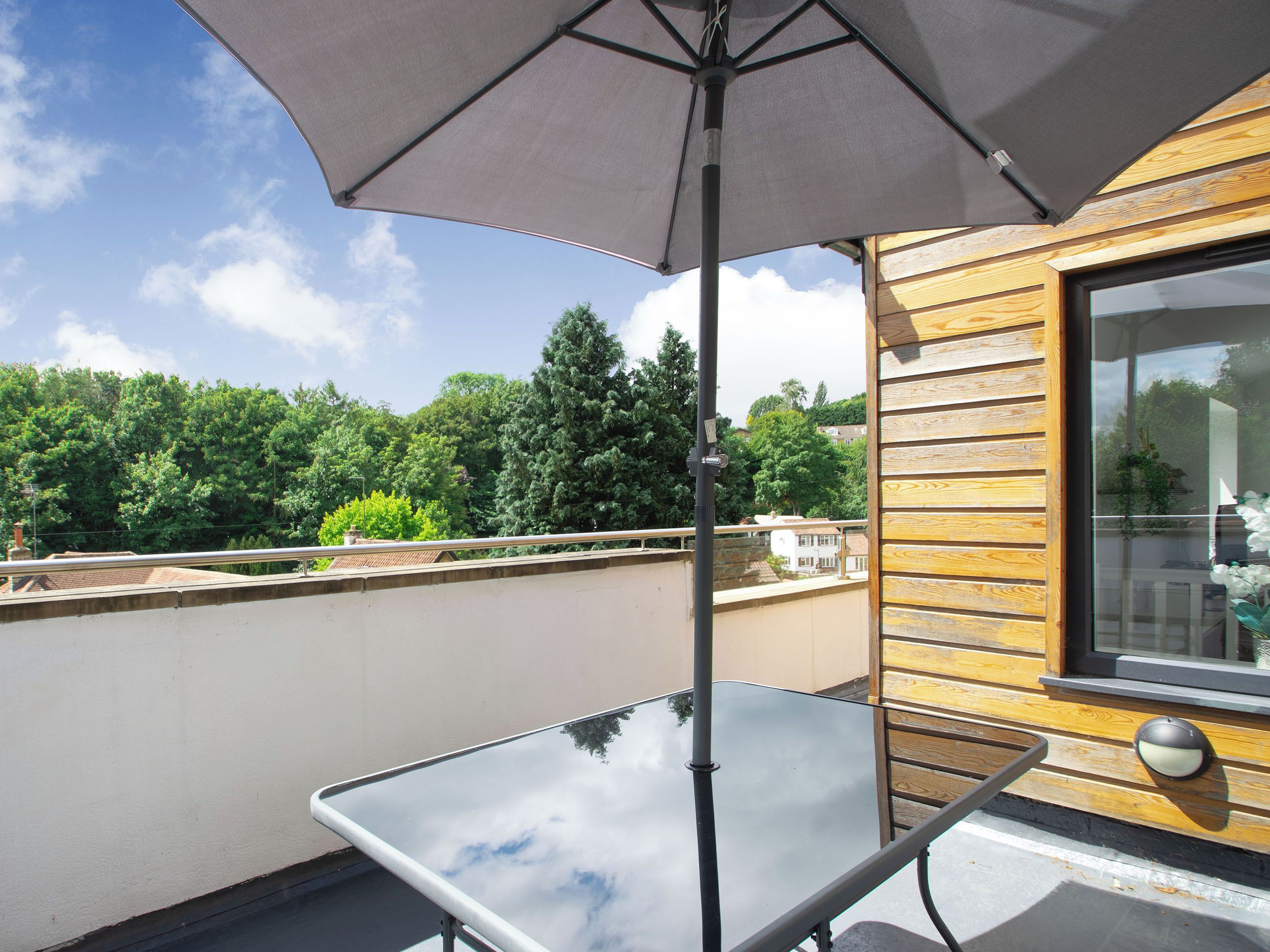 A balcony with a glass table, a wooden wall, and a large window.