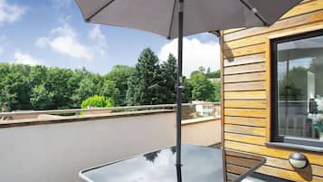 A balcony with a glass table, a wooden wall, and a large window.