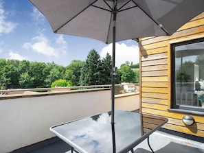 Un balcón con una mesa de vidrio, un muro de madera y un ventanal grande.