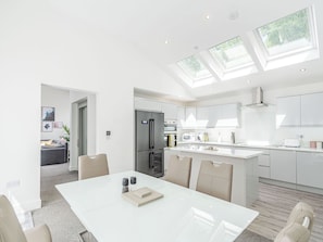 A modern kitchen with a central island, a dining area with a white table, and a living space with a sofa and artwork.