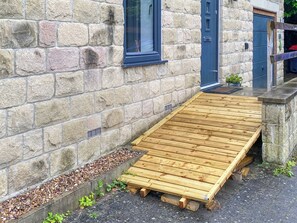 Une terrasse en bois attenante à un bâtiment en pierre, avec une fenêtre et une porte.
