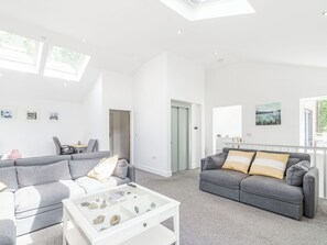 A spacious living area with a grey sofa, a coffee table with decorative items, and a view of the outdoors through large windows.