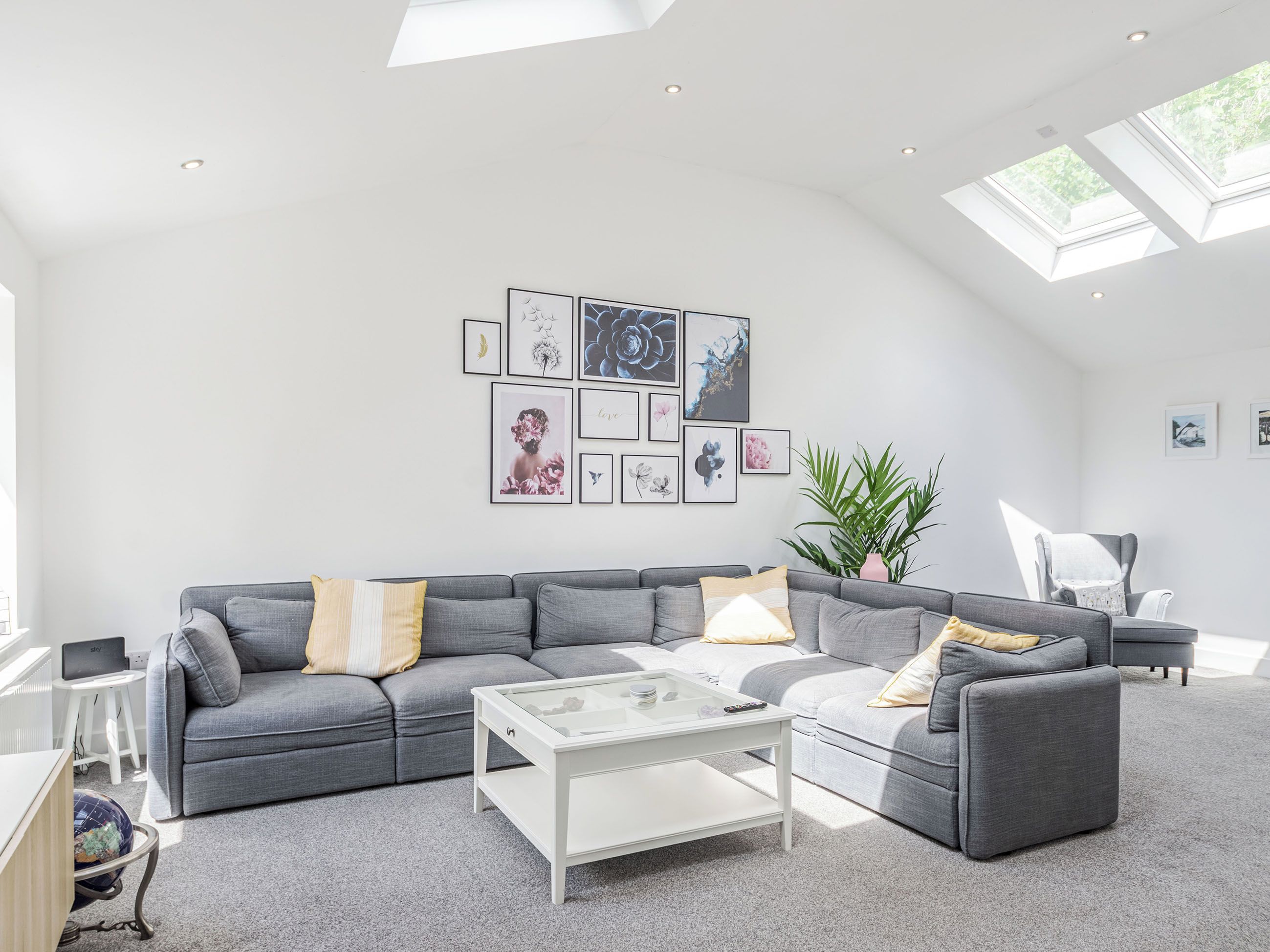 A modern living room with a grey sofa, a glass coffee table, and a skylight.