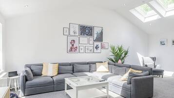 A modern living room with a grey sofa, a glass coffee table, and a skylight.
