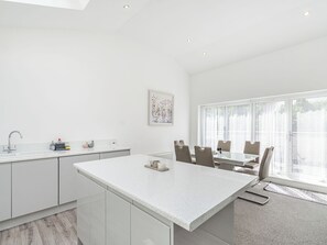 Una cocina moderna con una isla central, armarios blancos y una zona de comedor con mesa y sillas.