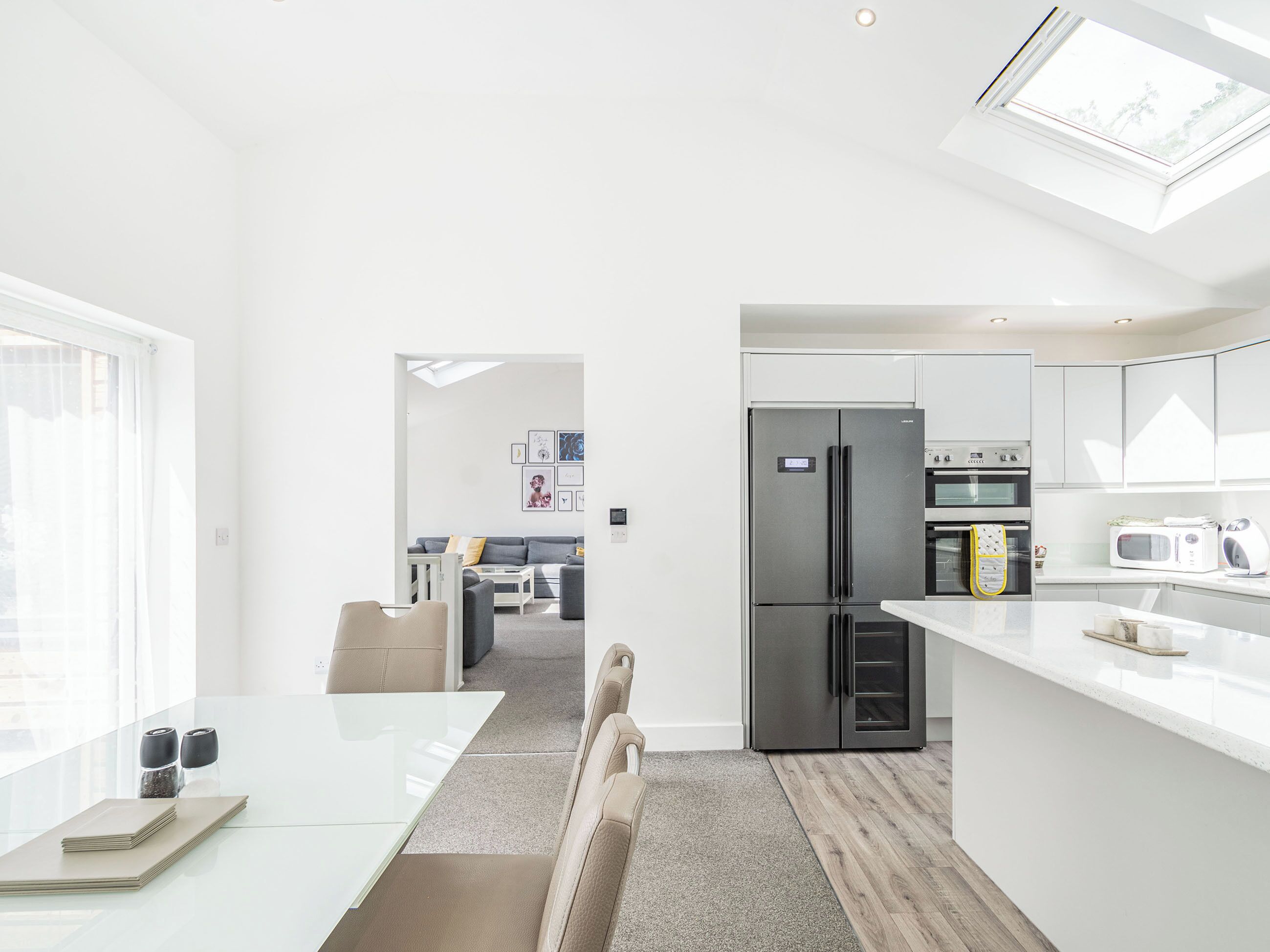 A modern kitchen with a built-in fridge, oven, and microwave, a dining area with a table and chairs, and a living room with a sofa and a coffee table.