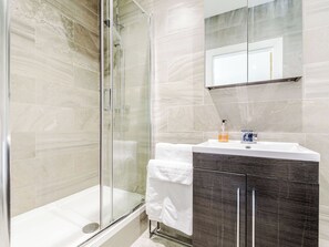 Un baño moderno con cabina de ducha de vidrio, lavabo blanco y tocador de madera oscura.