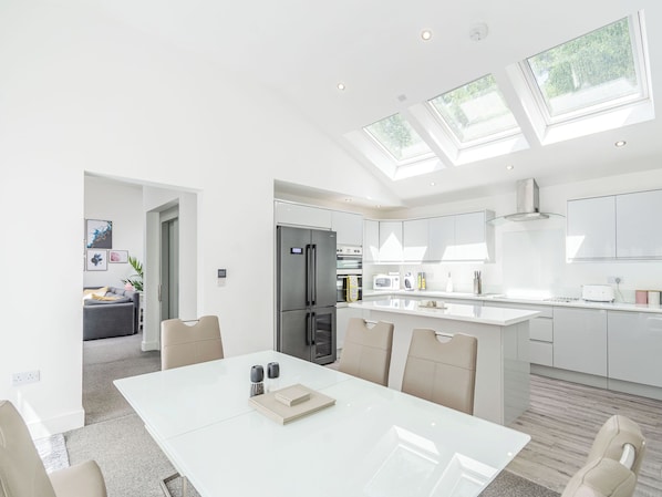 A modern kitchen with a central island, a dining area with a white table, and a living space with a sofa and artwork.