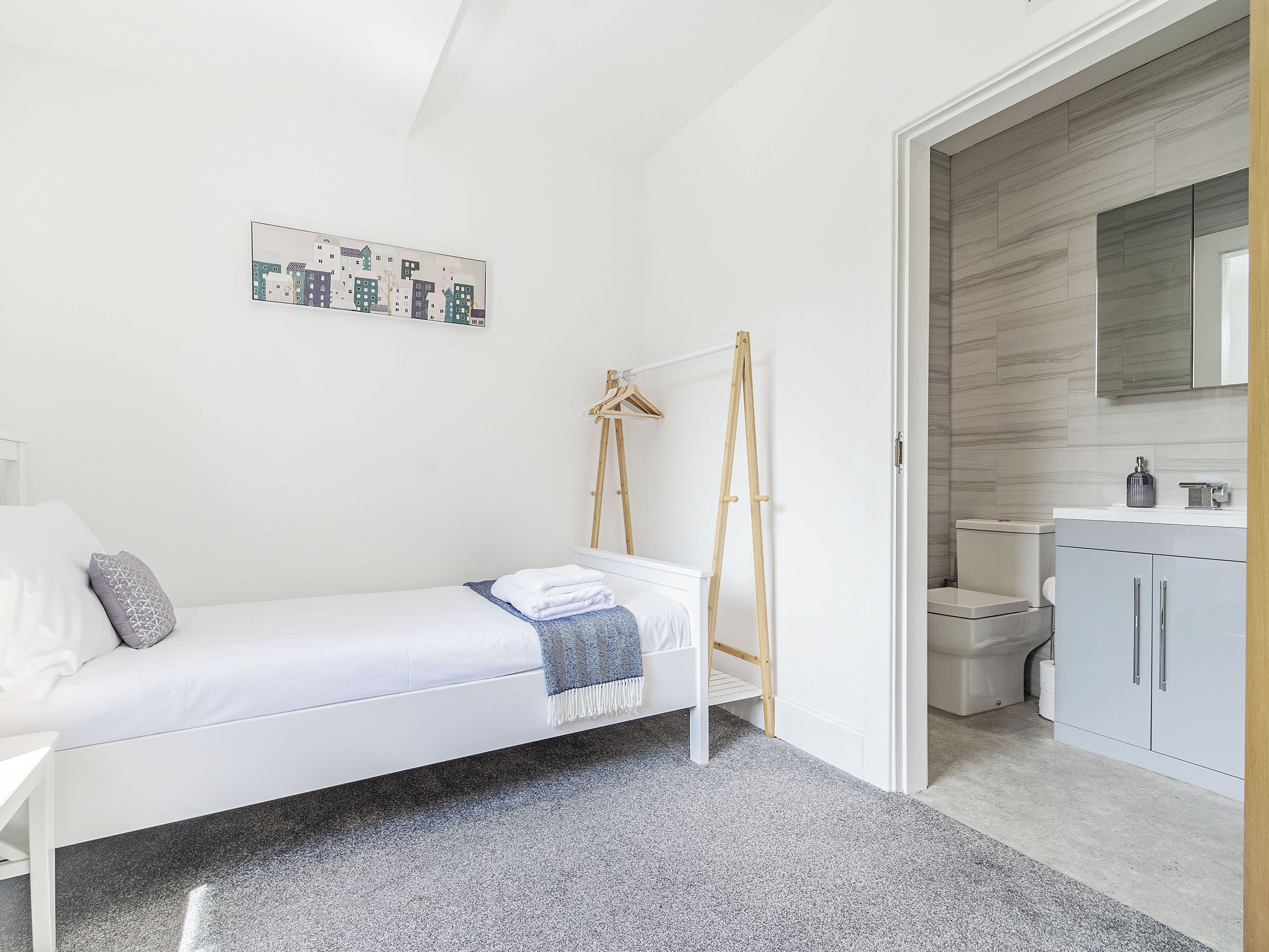 A bedroom with a bed, a wooden ladder, a white wardrobe, a bathroom with a toilet, and a wall-mounted mirror.