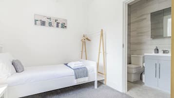 A bedroom with a bed, a wooden ladder, a white wardrobe, a bathroom with a toilet, and a wall-mounted mirror.