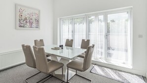 A modern meeting room with a glass table, four chairs, a radiator, a large window with curtains, and a floral artwork on the wall. - We love how modern and stylish High Trees View is. (Knaresborough, near Harrogate)