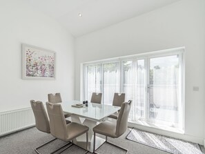 Una sala de reuniones moderna con una mesa de vidrio, cuatro sillas, un radiador, un amplio ventanal con cortinas y una obra de arte floral en la pared.