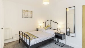 A bedroom with a bed, bedside tables, a wall-mounted lamp, a mirror, and a radiator. - We love how modern and stylish High Trees View is. (Knaresborough, near Harrogate)