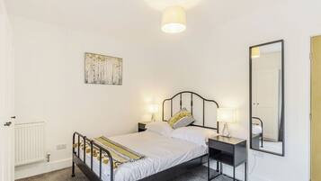 A bedroom with a bed, bedside tables, a wall-mounted lamp, a mirror, and a radiator.