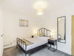 Un dormitorio con cama, mesitas de noche, una lámpara de pared, un espejo y un radiador.