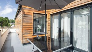 Moderni ulkoiluparveke, jossa on lasipöytä, puupanelointi ja suuri aurinkovarjo.