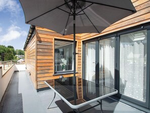 A modern outdoor balcony with a glass table, wooden paneling, and a large umbrella.